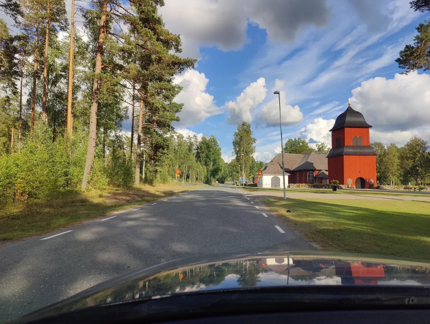 Road and wooded surroundings beside a red timber church in Sweden